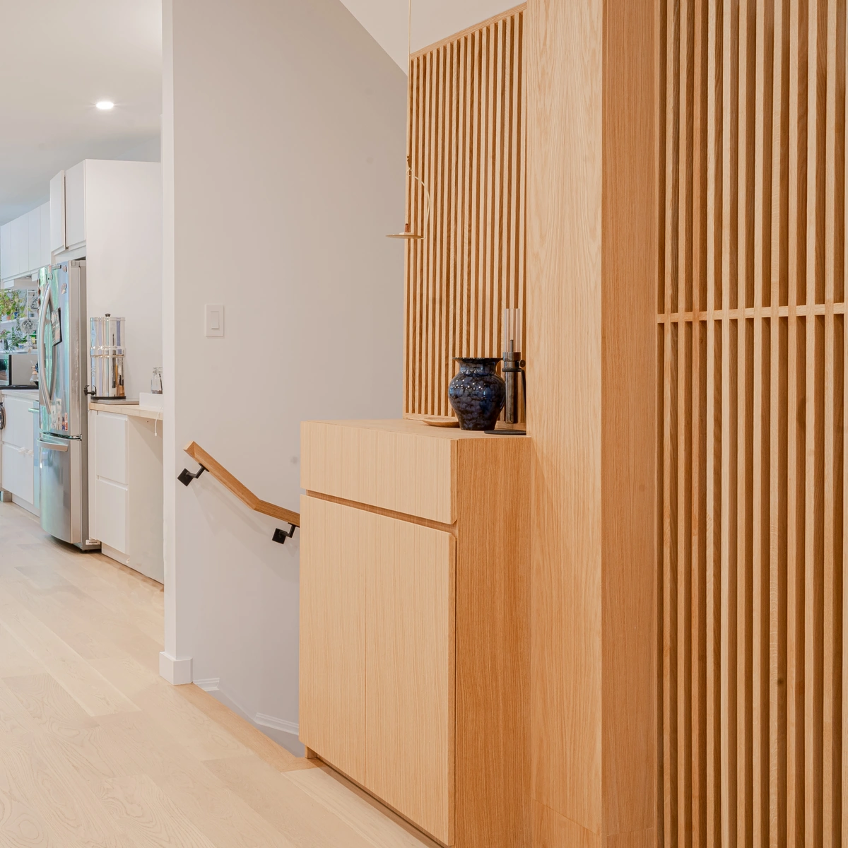 Vertical wood slats in light oak beside a staircase with a matching cabinet