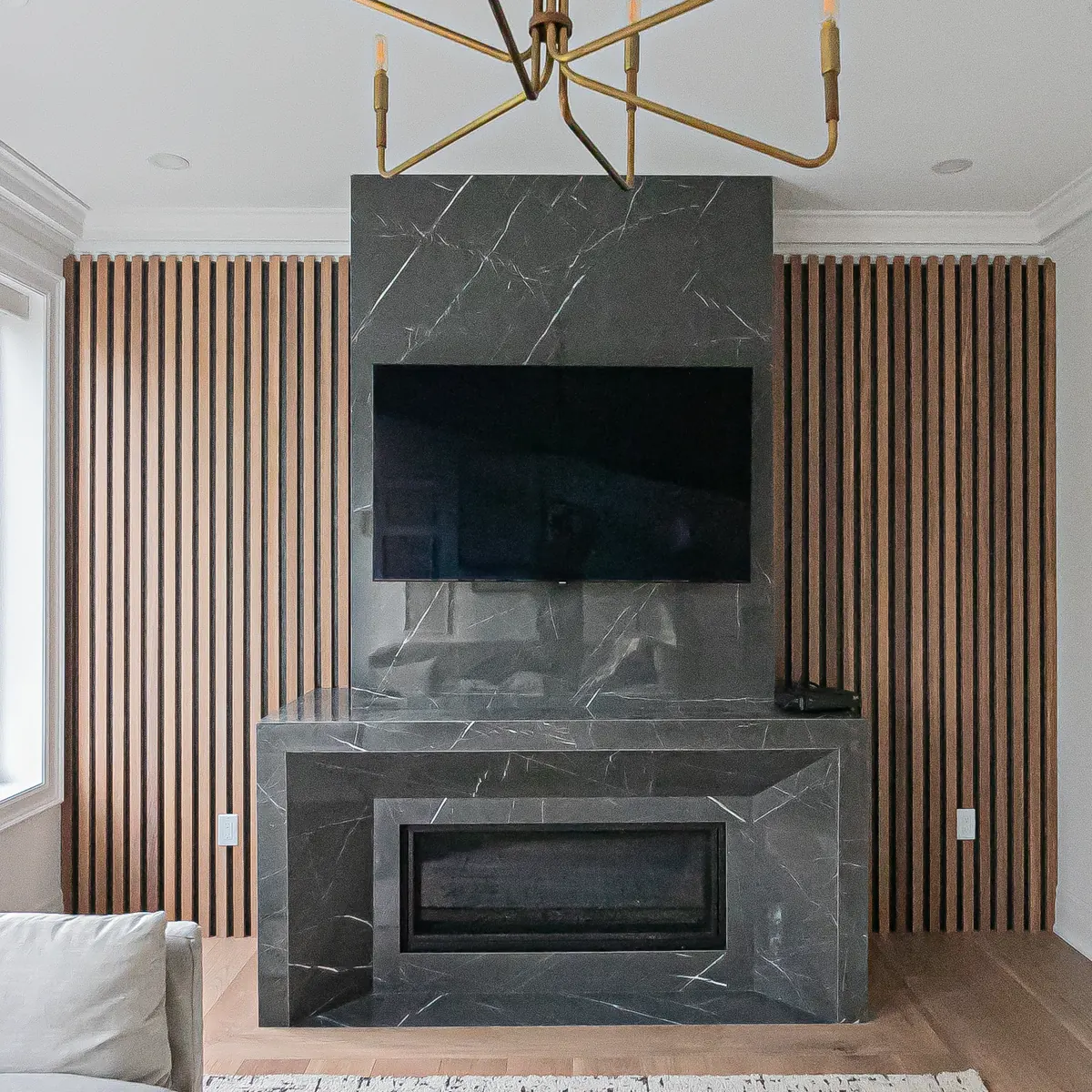 Wood slat wall panels on both sides of a dark stone fireplace and TV wall